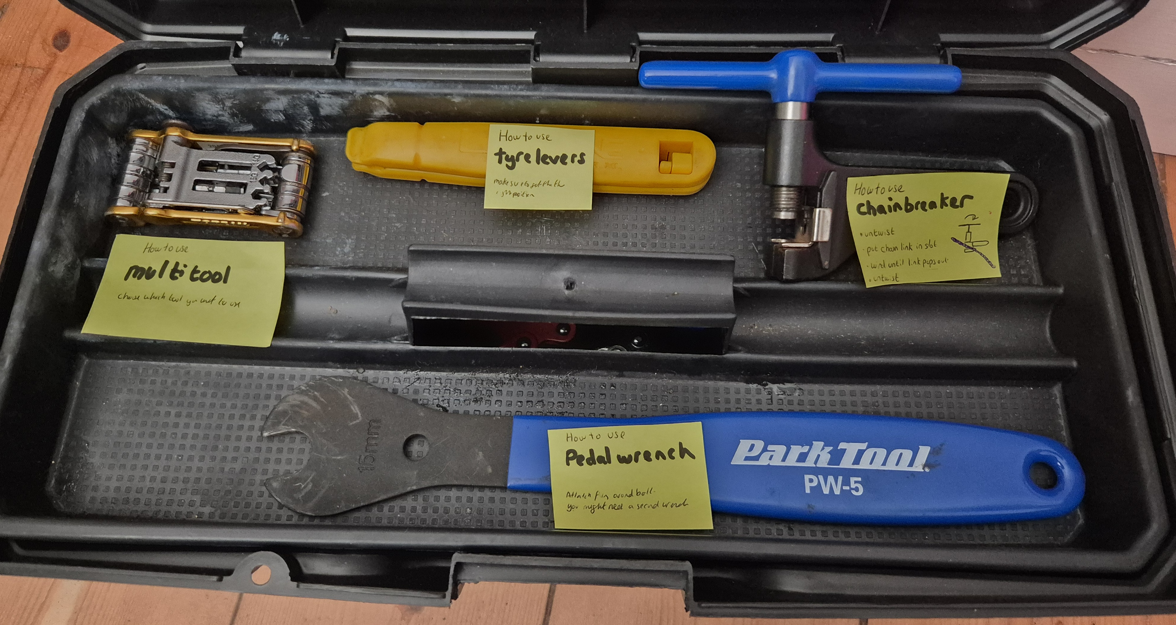 An open toolbox with a yellow label stuck to each bicycle maintenance tool that is on the tray. Each label gives the name of that tool and a description of how to use the tool.