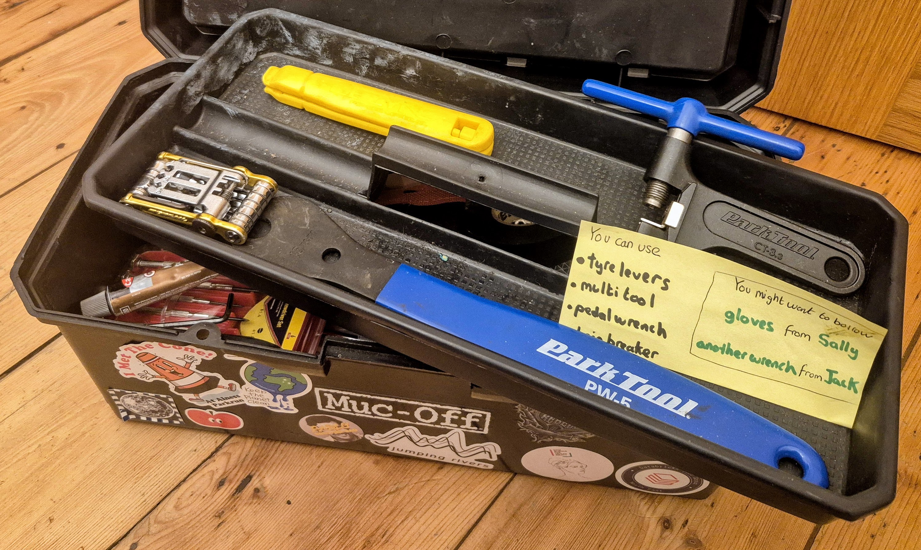 The open toolbox shows a tray of 4 tools at the top, with a single label stating the names of the 4 tools you can use. The label also advises that you might need to borrow gloves from Sally and another wrench from Jack. The tray sits at an angle allowing a glimpse at a collection of tools hiding at the bottom of the toolbox.
